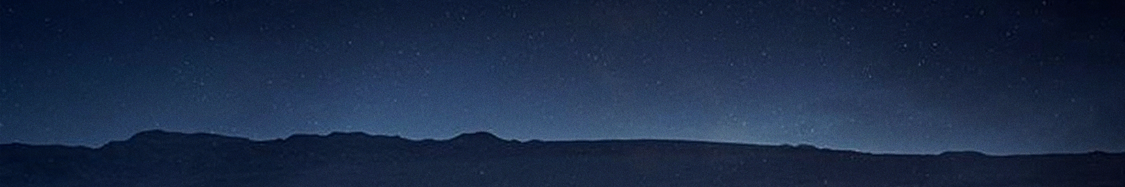 Un ciel de nuit bleu foncé, rempli d’étoiles, s’étend au-dessus de la silhouette d’une chaîne de montagnes lointaine