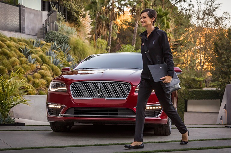 Une femme qui marche devant un véhicule Lincoln rouge