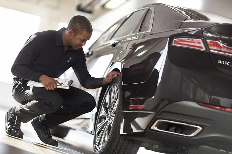 Un technicien d'entretien Lincoln inspecte la bande de roulement d'un pneu d'un Lincoln MKZ