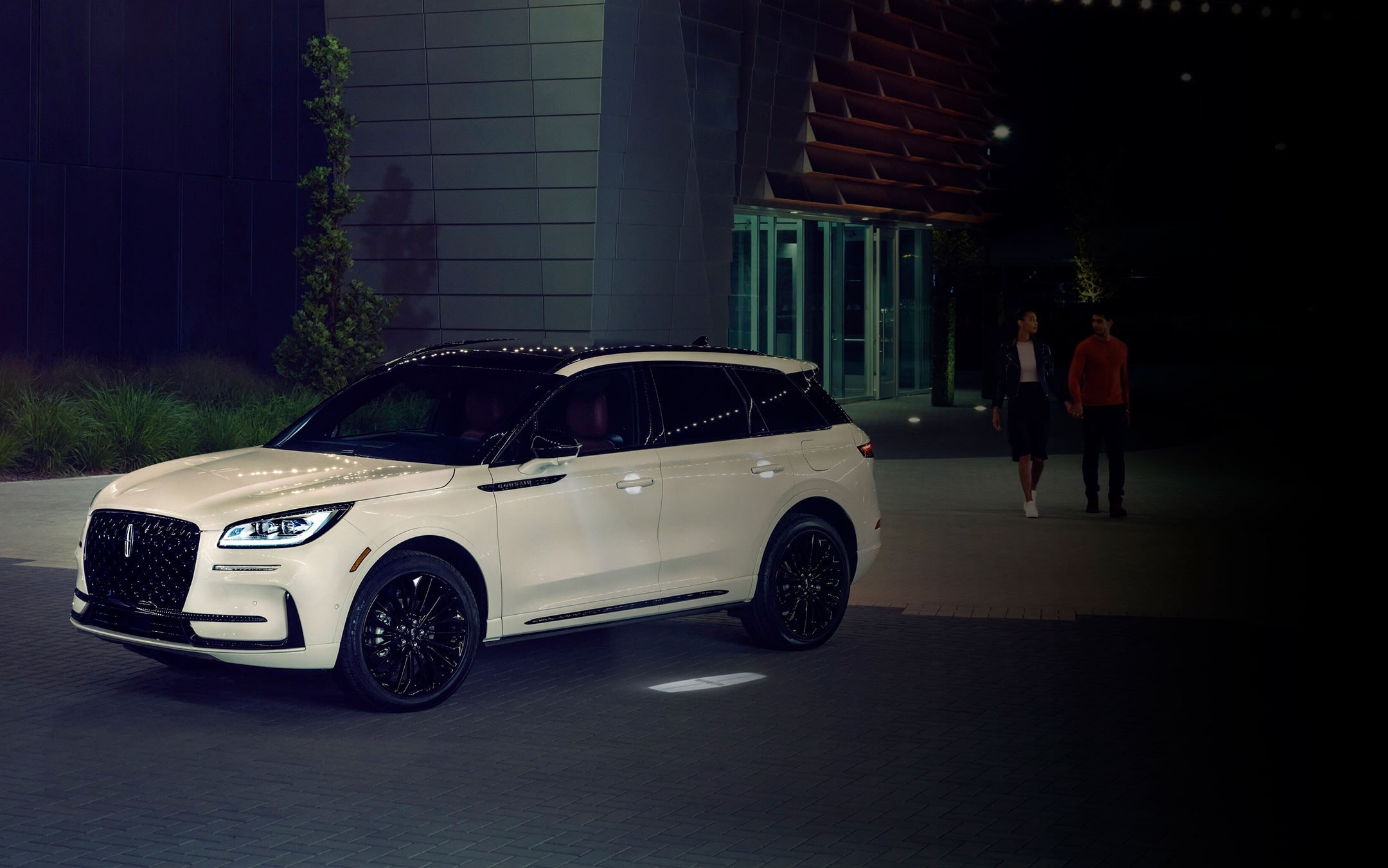 Un couple s’approche d’un Lincoln Corsair 2025 alors que l’éclairage Lincoln Embrace guide le chemin