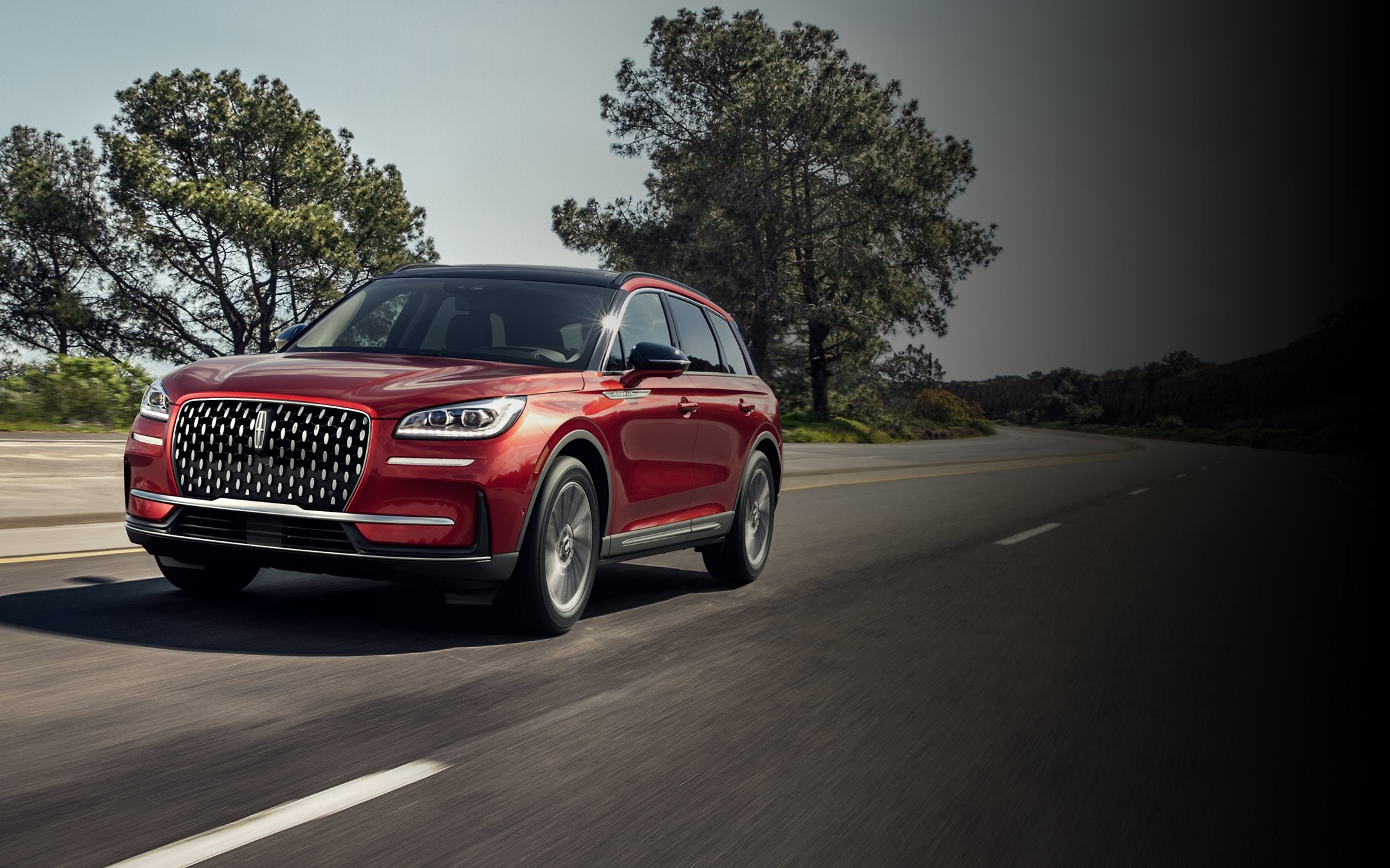 Un Lincoln Corsair 2025 de couleur extérieure tapis rouge est conduit sur une route de campagne
