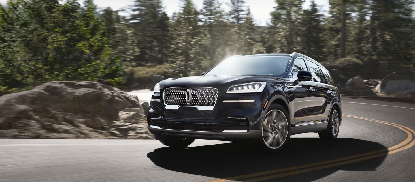 Un Lincoln Aviator noir dans un virage sur une route de montagne, avec des conifères et des rochers en arrière-plan.