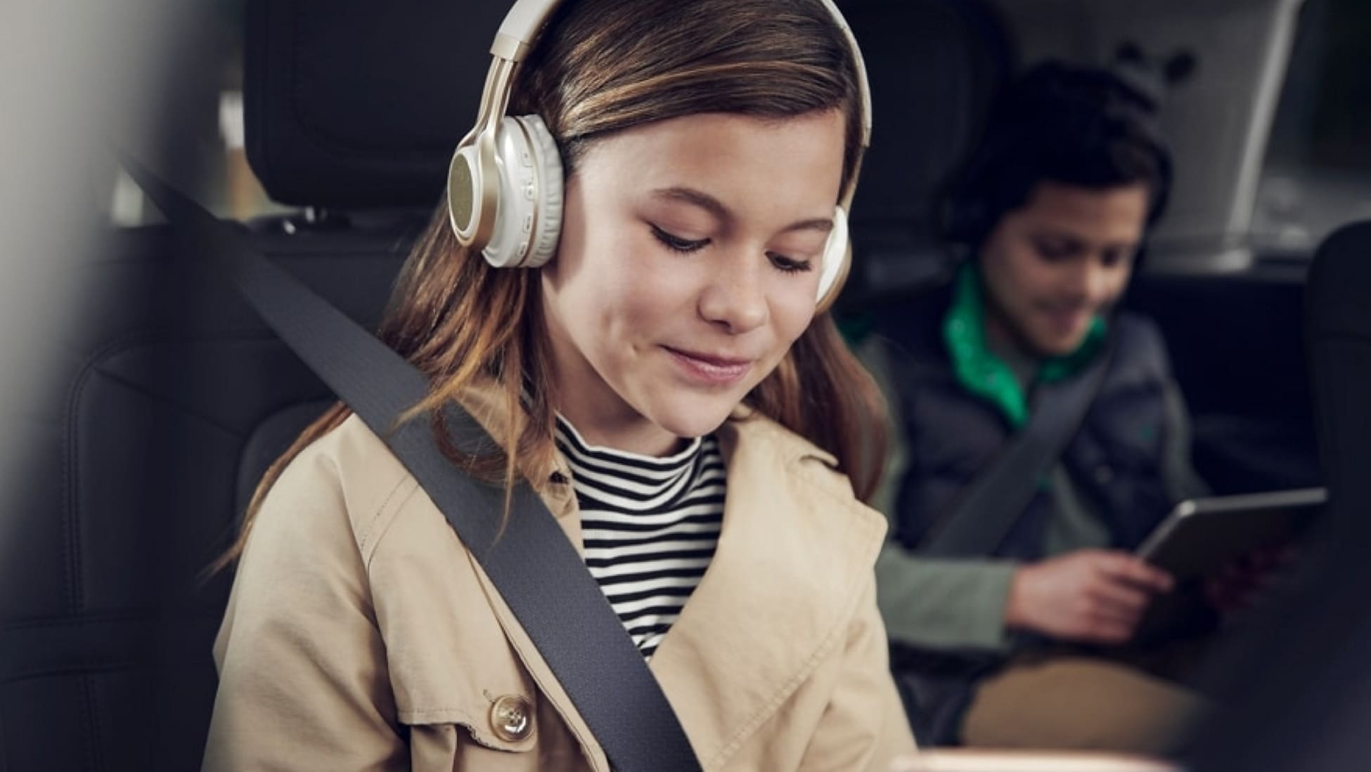 Deux enfants portant des écouteurs et regardant des appareils mobiles sont assis dans les sièges passagers d’un véhicule Lincoln.