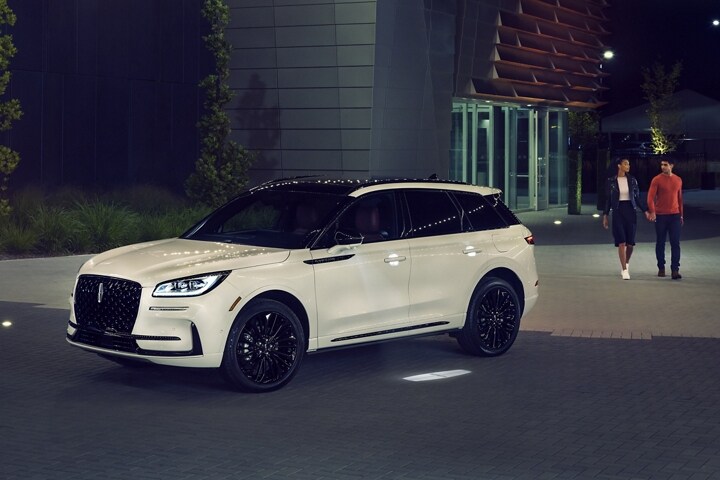 Un couple s’approche d’un Lincoln Corsair 2025 alors que l’éclairage Lincoln Embrace guide le chemin