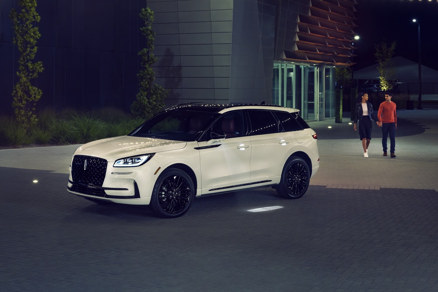 Un couple s’approche d’un VUS Lincoln Corsair 2026 alors que l’éclairage Lincoln Embrace guide le chemin