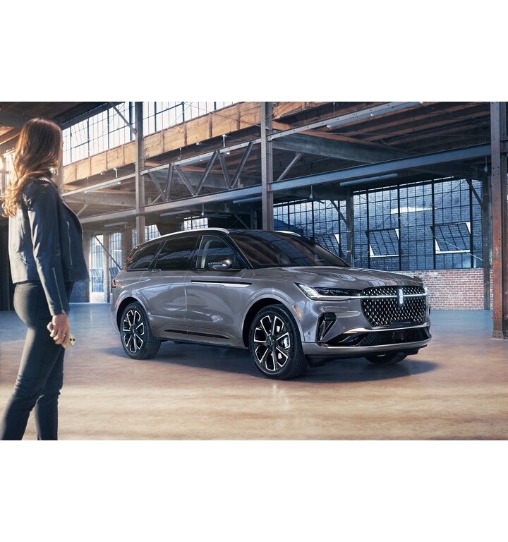 Un téléphone intelligent est tenu dans la main d’une femme alors qu’elle marche vers un VUS Lincoln Black Label Nautilus 2025