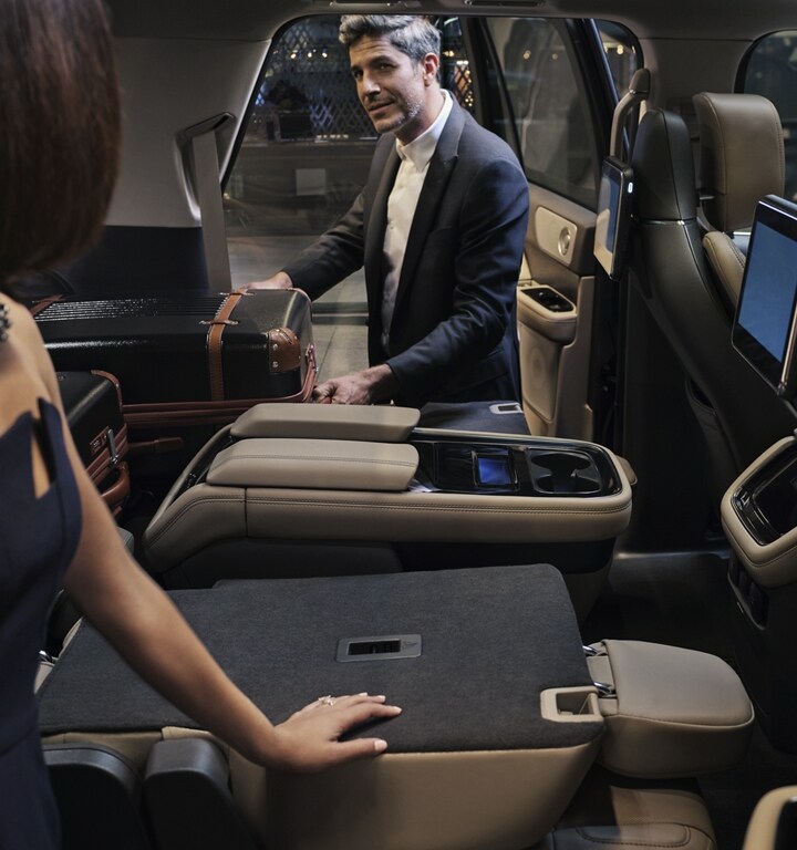 Un homme sort une valise du siège de la deuxième rangée repliée à plat d’un VUS Lincoln Navigator® 2023